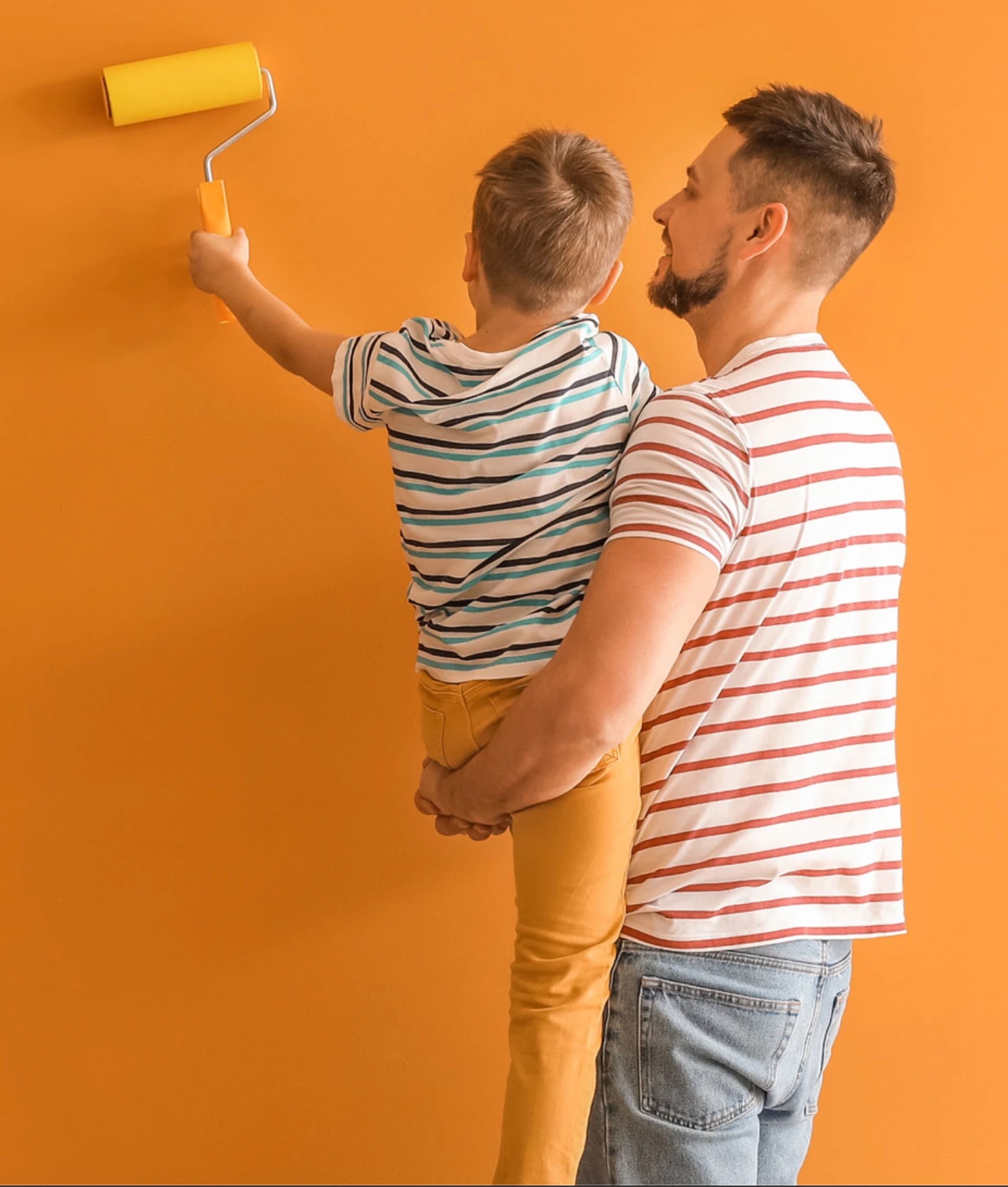 Father lifting his son to paint the wall with a yellow roller
