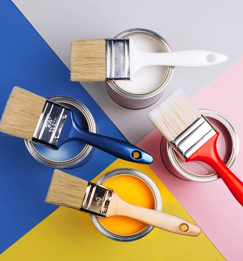 Paint brushes resting on open tins of white, blue, yellow and red paint