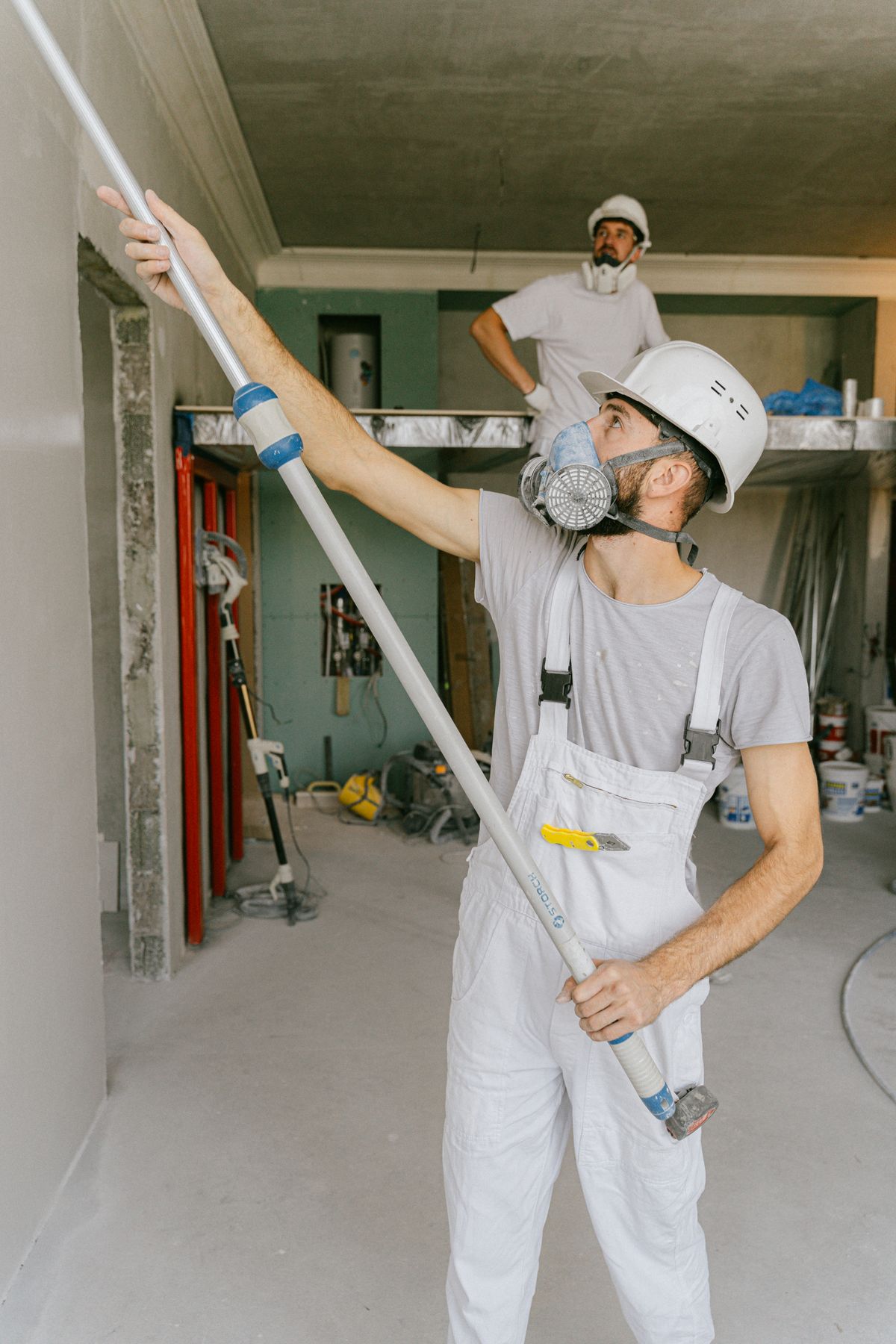 Professional painter in safety gear rolling an interior wall on a renovation site