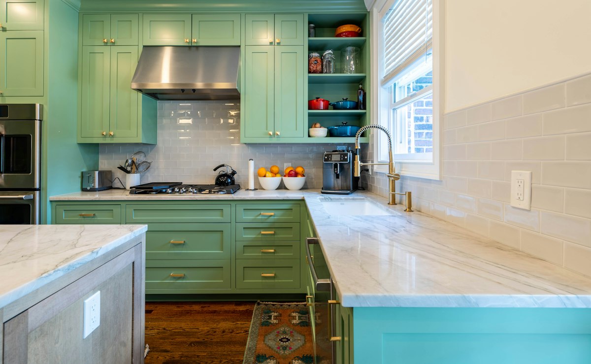 Kitchen with sage green painted cabinets and marble worktops