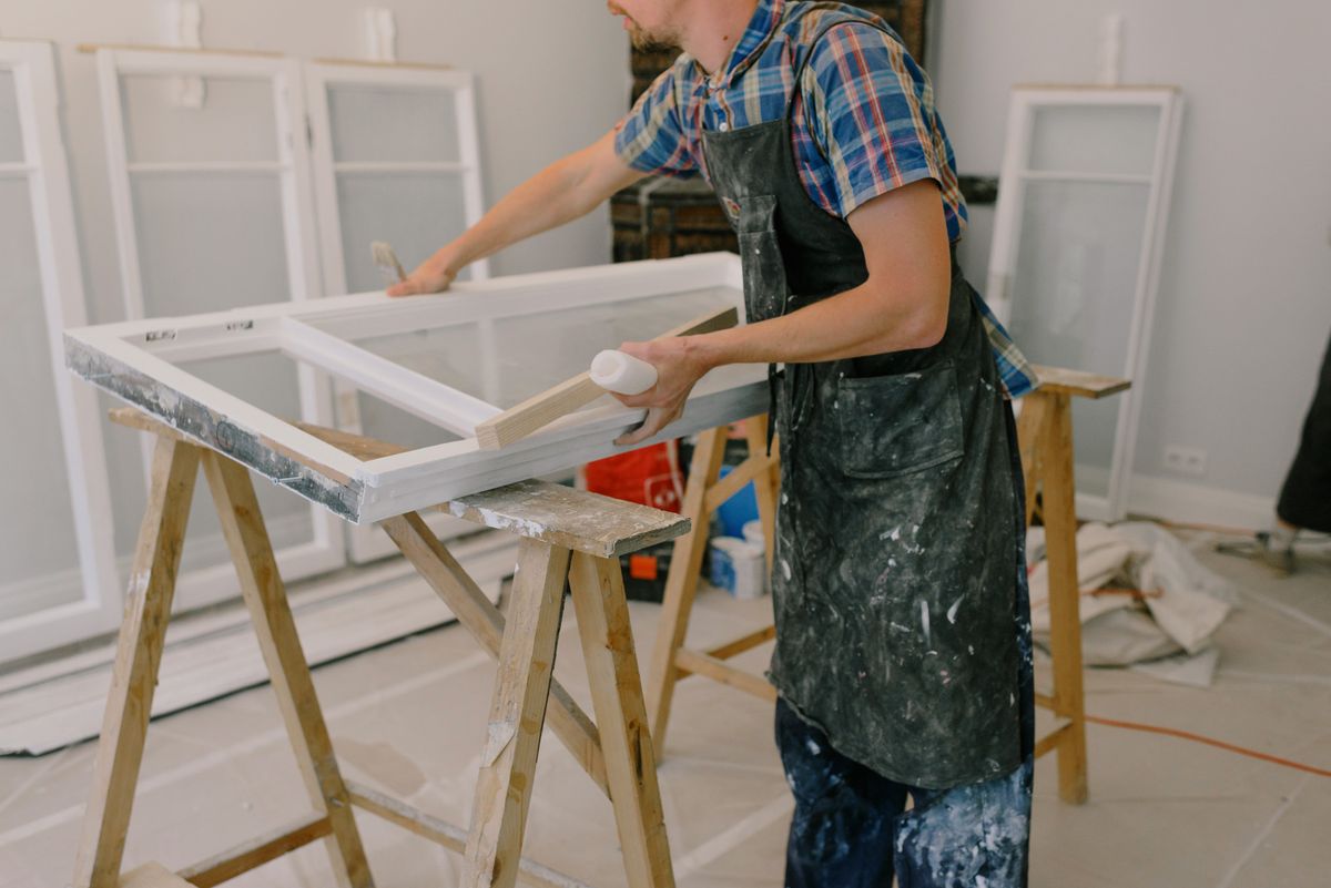 Craftsman restoring a white timber window frame on trestles